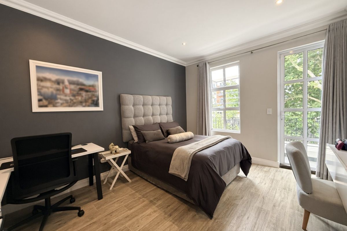 A well-maintained bedroom featuring modern laminate flooring, crown molding, recessed lighting, and large windows providing natural light and balcony access.