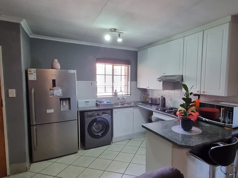 A functional kitchen featuring white cabinetry, dark laminate countertops, tiled flooring, and integrated appliances including a hob and extractor fan.