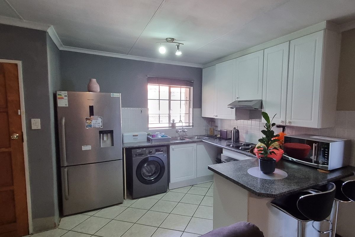 A functional kitchen featuring white cabinetry, dark laminate countertops, tiled flooring, and integrated appliances including a hob and extractor fan.