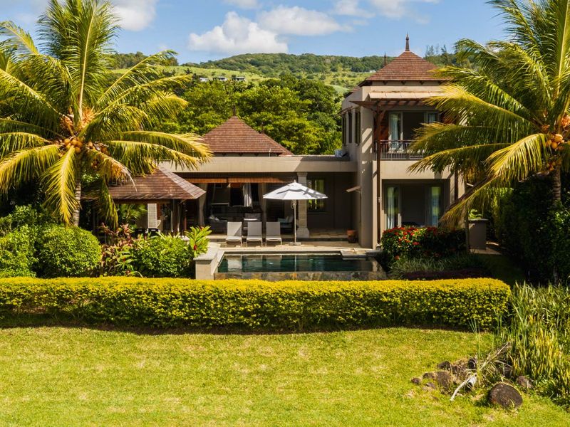 A beautiful rear exterior view of a two-story villa featuring a private swimming pool, covered patio, and lush tropical landscaping.