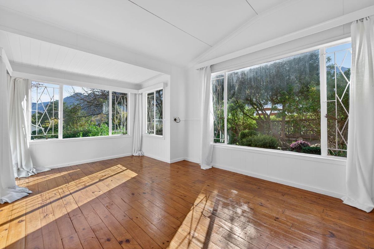 Bright and airy living room featuring polished timber flooring, large windows with garden views, and a classic tongue and groove ceiling.