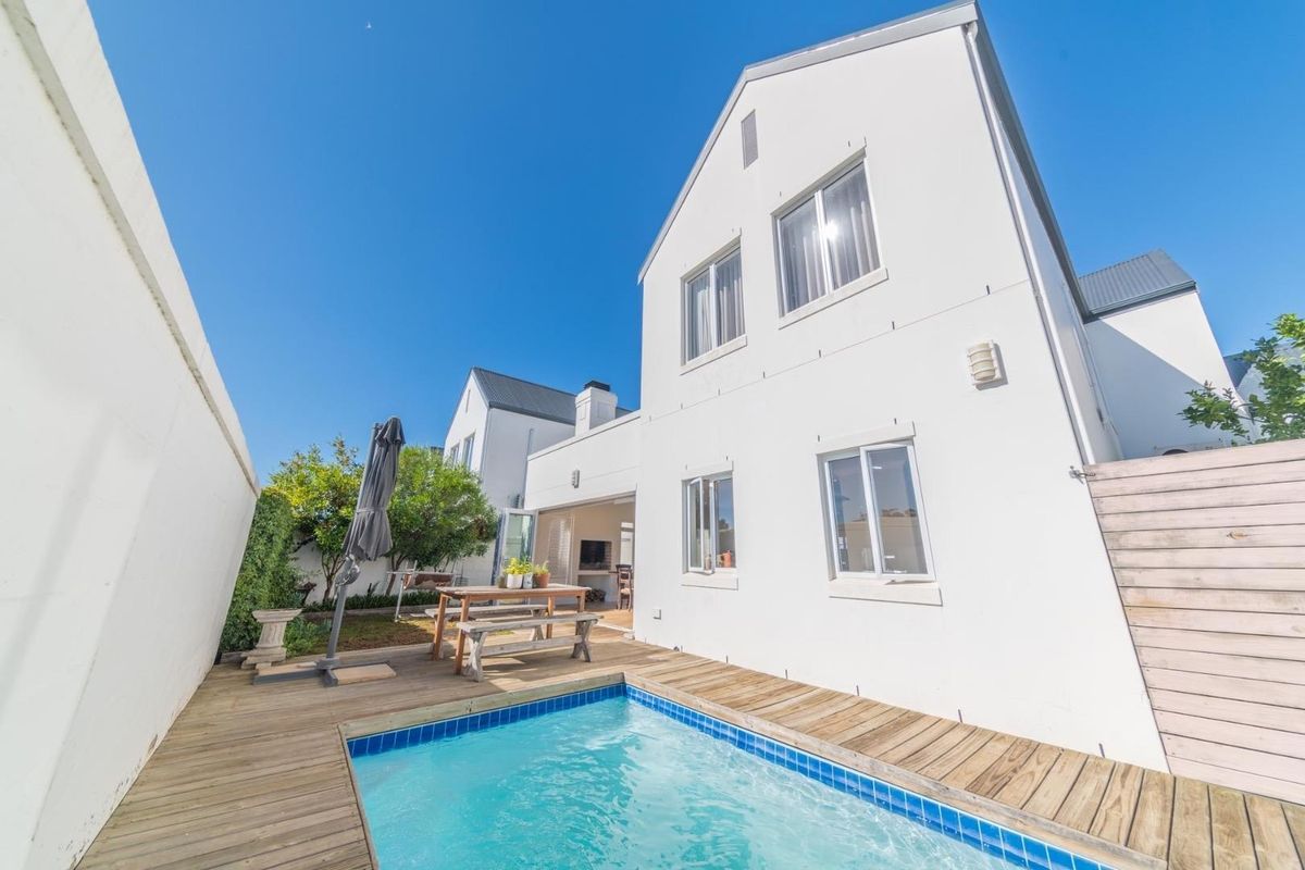 Rear exterior view of the house featuring a swimming pool, wooden decking, and a white facade with large windows.