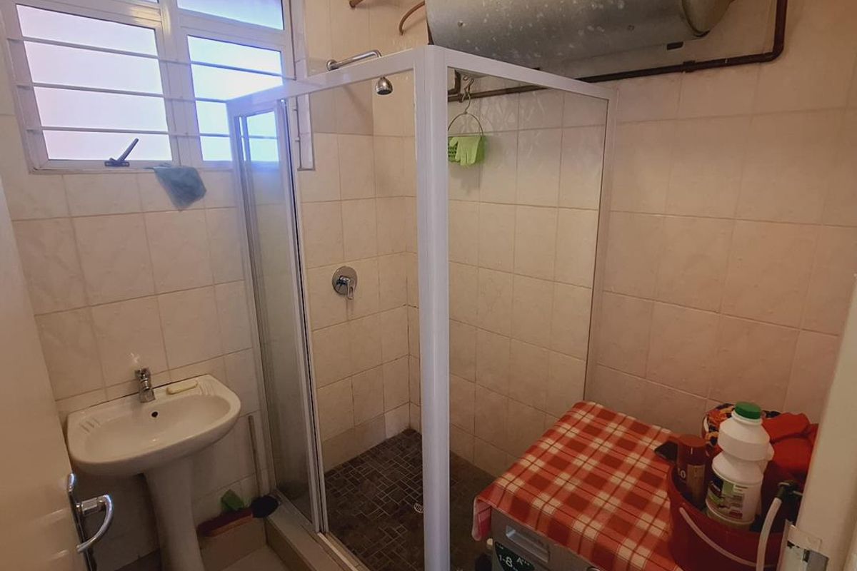 Compact bathroom featuring a pedestal basin, shower enclosure, and tiled finishes, with an integrated laundry area and exposed geyser unit.