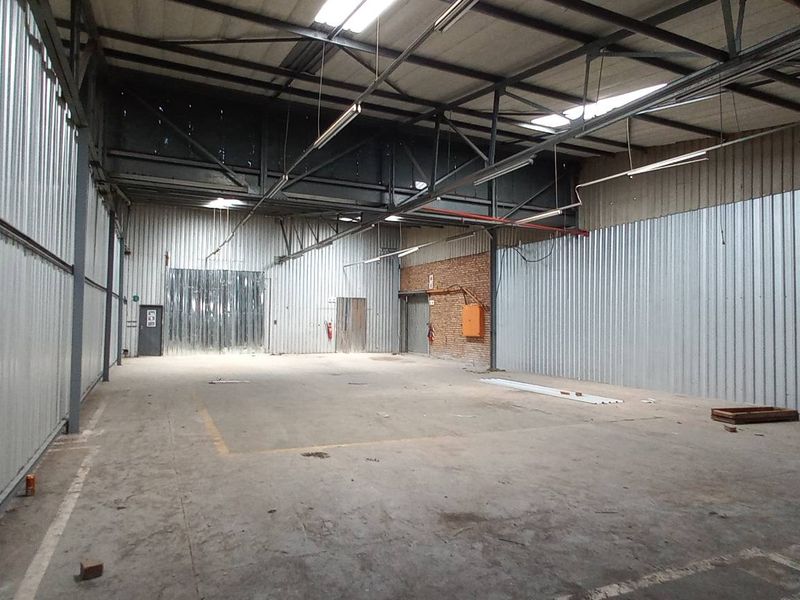 Spacious industrial warehouse unit featuring high ceilings with exposed steel trusses, corrugated metal walls, and durable concrete flooring.