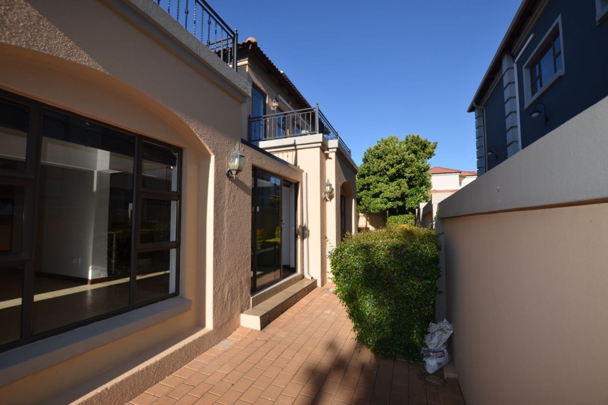 A view of the rear exterior of the house, featuring a paved patio area, sliding glass doors, and an upper-level balcony with wrought iron railings.