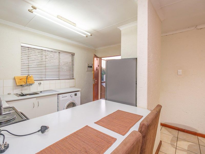 Compact kitchen featuring built-in cabinetry, a stainless steel sink, tiled backsplash, and a built-in hob, with direct access to the exterior.