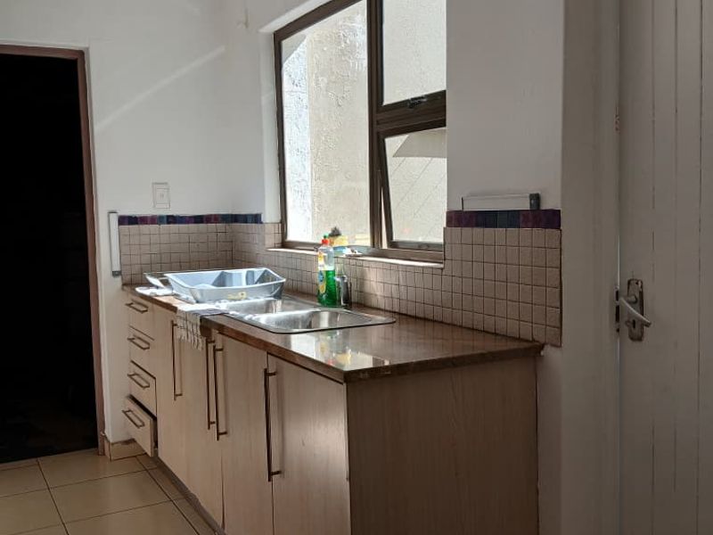 A functional kitchen area featuring a stainless steel double sink, laminate cabinetry, and tiled splashbacks, ready for modernization.