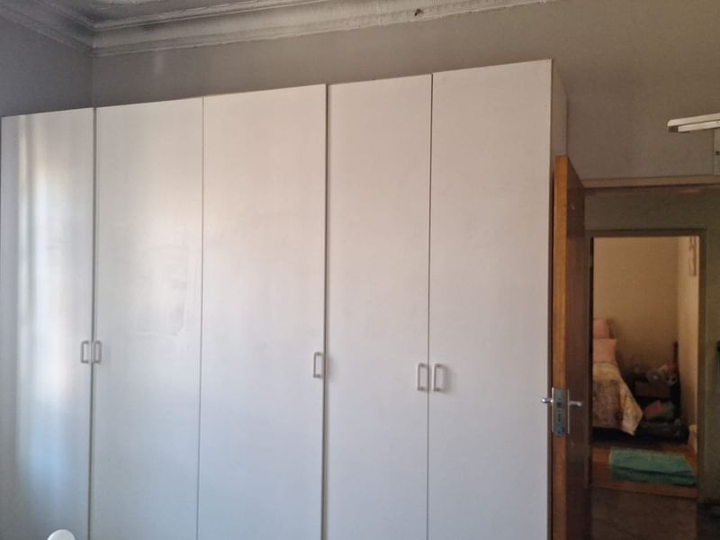 A bedroom featuring white built-in cupboards and decorative ceiling cornicing, with a view into an adjacent room.
