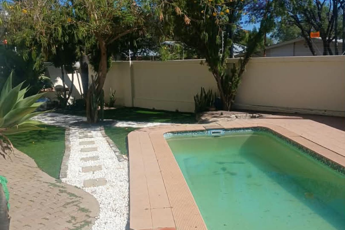 Outdoor pool area featuring a swimming pool with tiled coping, surrounded by a paved walkway, artificial grass, and a perimeter boundary wall.