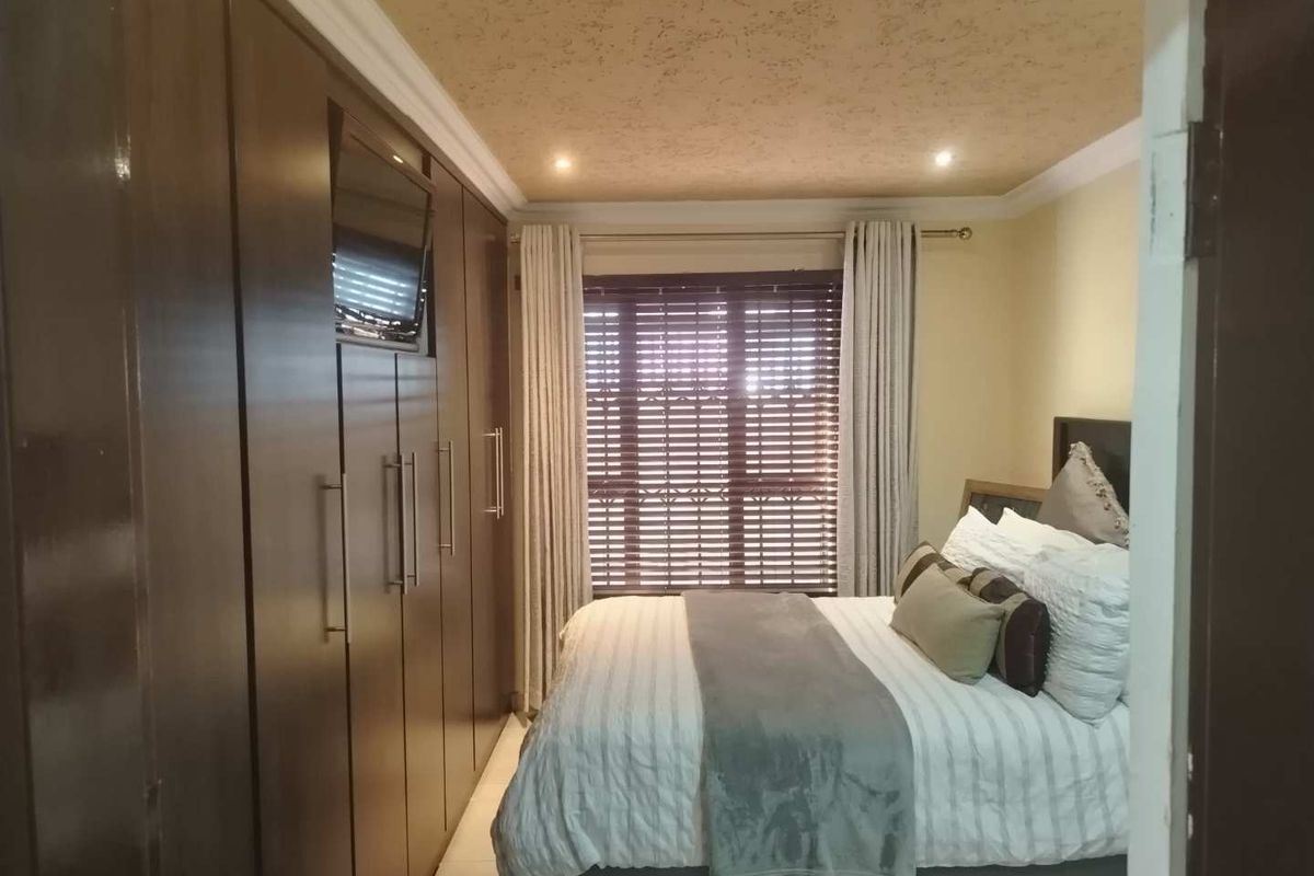 A well-maintained bedroom featuring extensive floor-to-ceiling built-in cupboards, recessed ceiling lighting, and large windows with fitted venetian blinds.