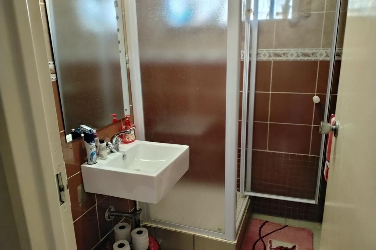 Compact bathroom featuring a wall-mounted basin, shower enclosure with frosted glass door, and brown tiled walls.