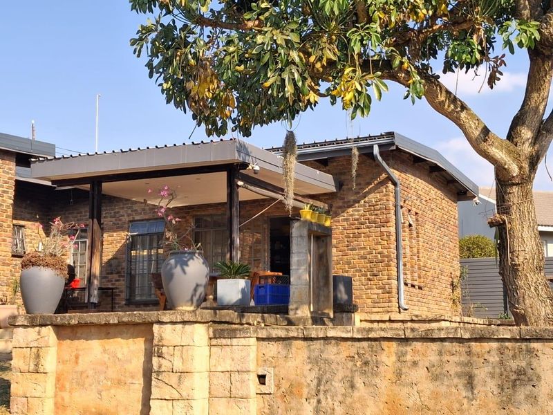 A charming exterior view of a brick-clad home featuring a covered patio area and a stone retaining wall, set under a mature tree.