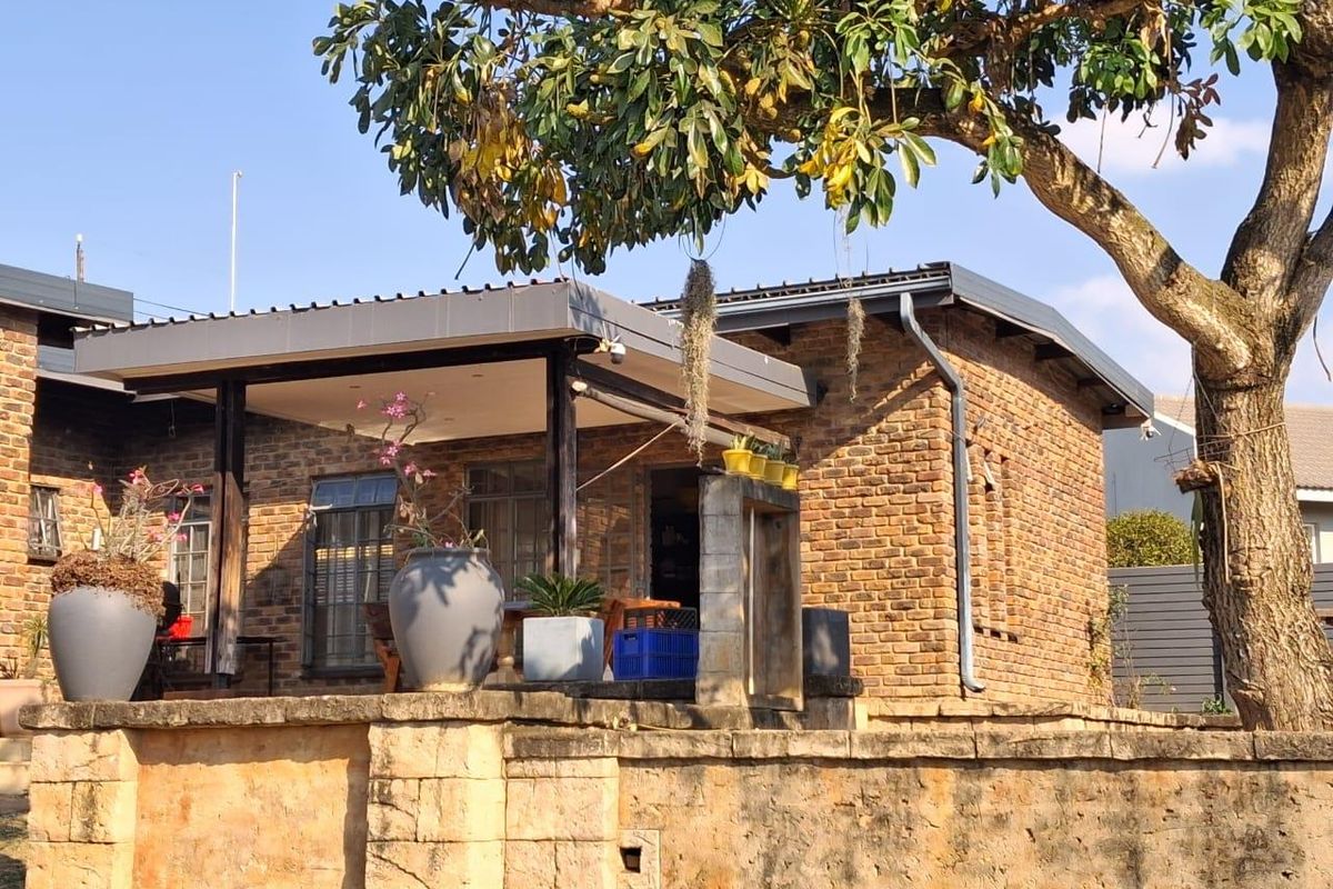 A charming exterior view of a brick-clad home featuring a covered patio area and a stone retaining wall, set under a mature tree.