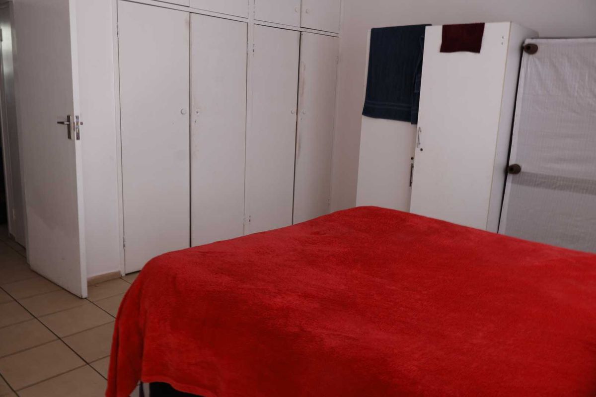A bedroom featuring built-in cupboards and tiled flooring, offering a functional space with neutral finishes.
