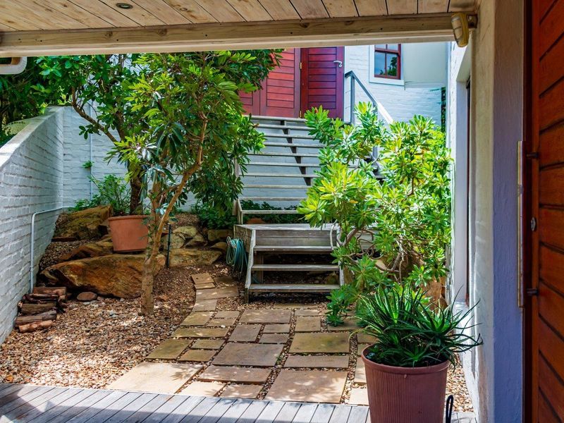 A covered timber deck overlooking a landscaped garden area with a stone pathway and timber staircase leading to the main entrance.