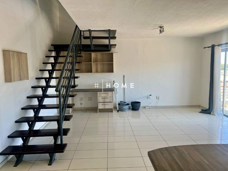 Open plan living area featuring a modern metal staircase, built-in desk with shelving, and neutral tiled flooring leading to a sliding glass door.