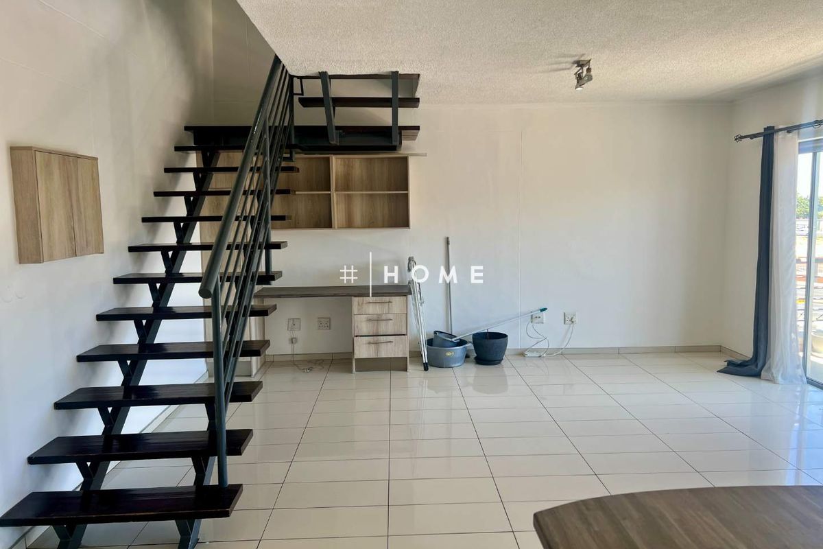 Open plan living area featuring a modern metal staircase, built-in desk with shelving, and neutral tiled flooring leading to a sliding glass door.