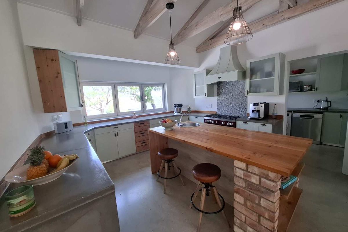Spacious kitchen featuring a central island with a timber countertop, exposed timber ceiling beams, concrete work surfaces, and a separate scullery area.