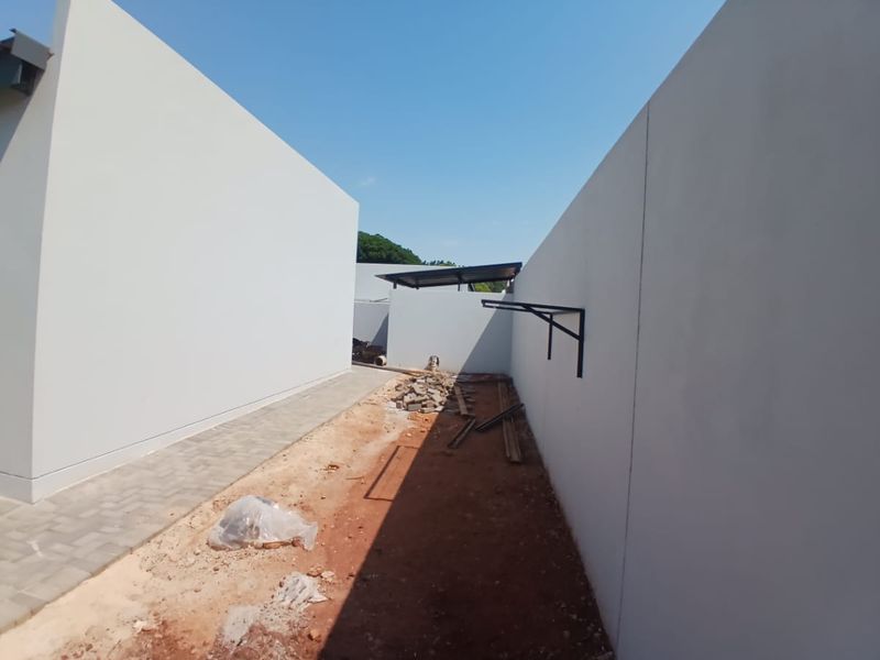 An unfinished rear exterior area featuring paved walkways and boundary walls, currently awaiting landscaping and final site clearance.