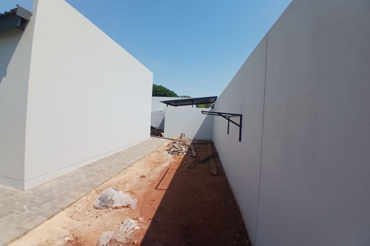 An unfinished rear exterior area featuring paved walkways and boundary walls, currently awaiting landscaping and final site clearance.