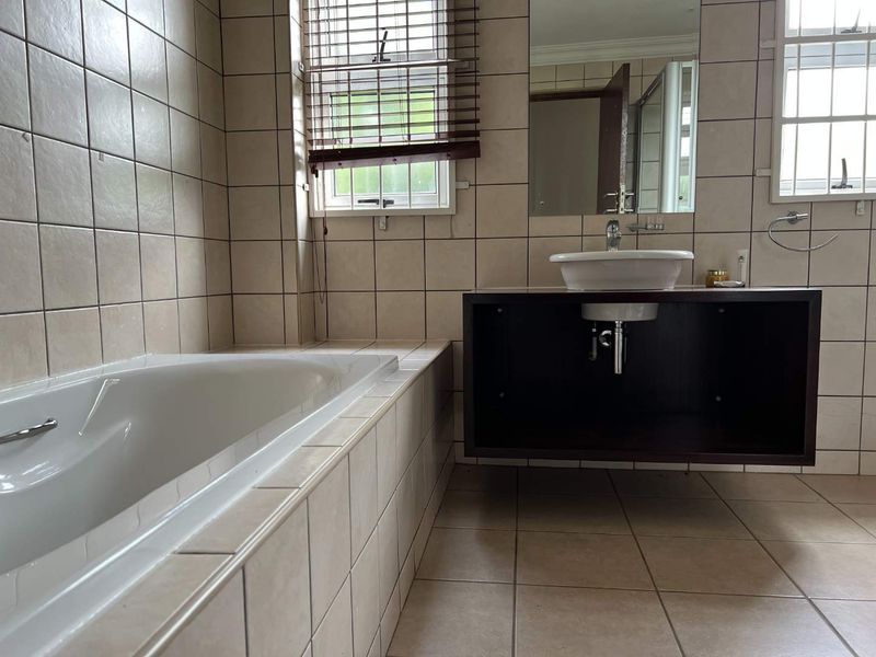 A functional bathroom featuring a built-in bathtub, a floating vanity with a vessel sink, and neutral wall and floor tiling.