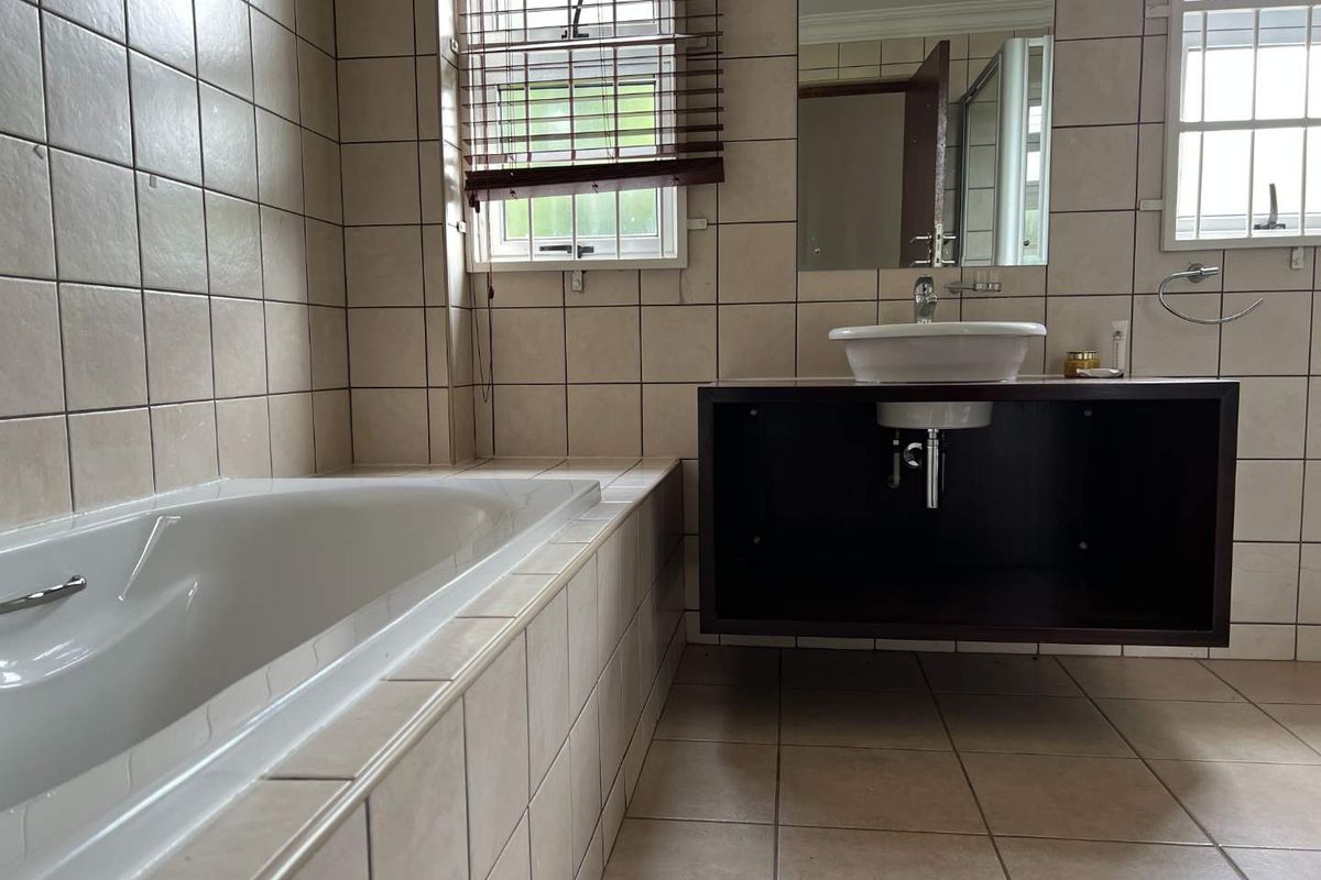 A functional bathroom featuring a built-in bathtub, a floating vanity with a vessel sink, and neutral wall and floor tiling.