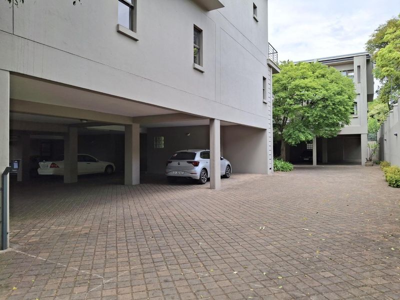 A view of the townhouse complex showing a paved driveway leading to covered parking bays and building exterior.
