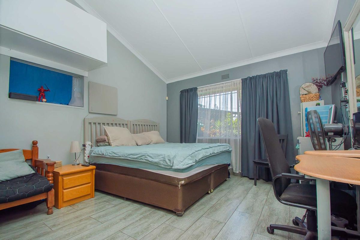 A bedroom featuring vaulted ceilings, laminate flooring, and a window with curtain tracks, offering a functional space with potential for modern updates.