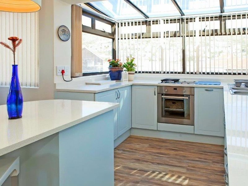 Bright kitchen featuring light blue cabinetry, stone countertops, built-in oven, and a glass roof conservatory providing ample natural light.
