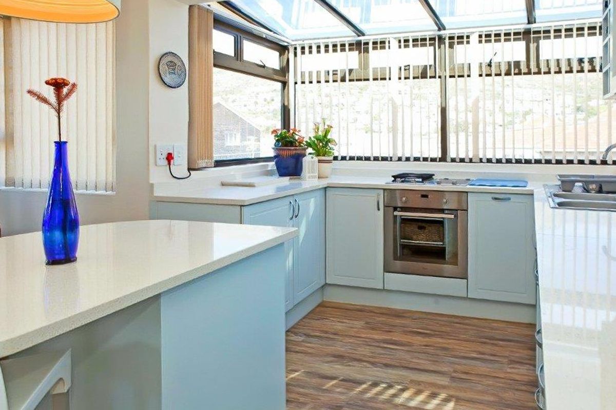 Bright kitchen featuring light blue cabinetry, stone countertops, built-in oven, and a glass roof conservatory providing ample natural light.