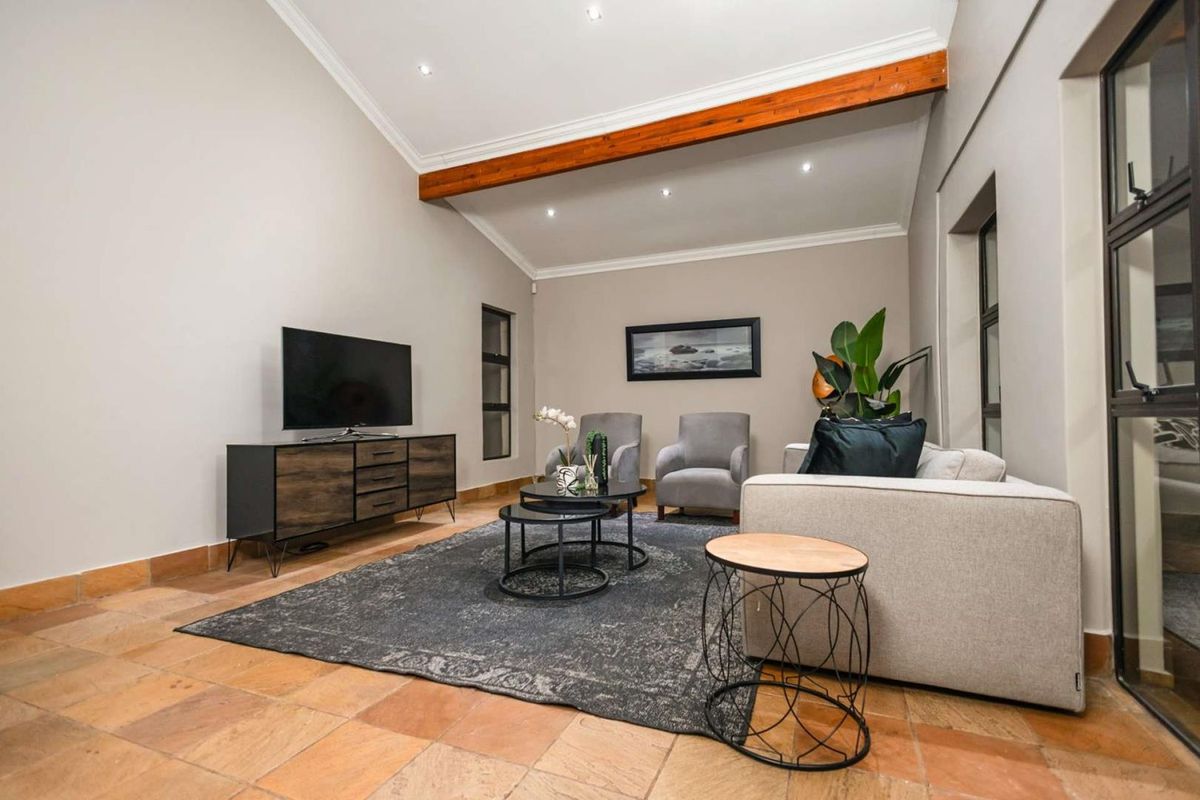 Spacious living room featuring high vaulted ceilings with exposed timber beams, recessed downlighting, and durable terracotta-style tiled flooring.
