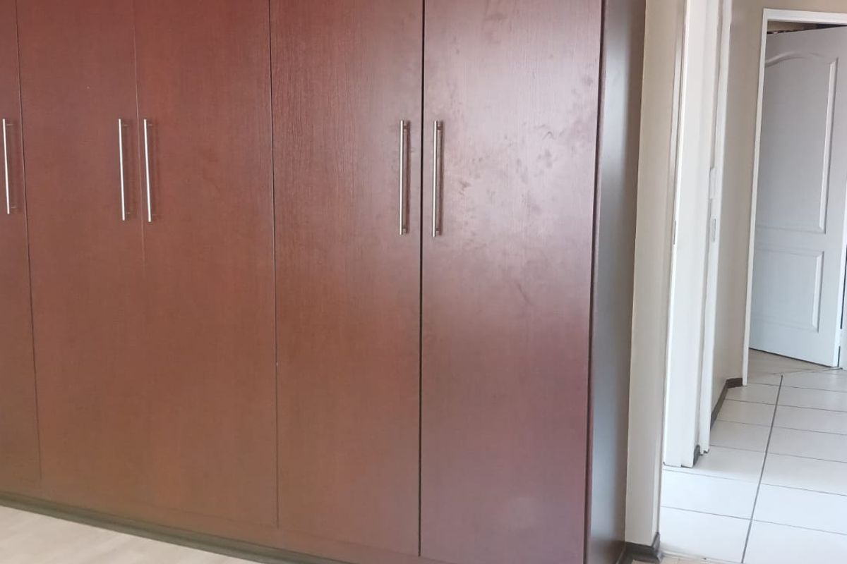 A bedroom featuring built-in wooden cupboards, laminate flooring, and access to a tiled hallway.