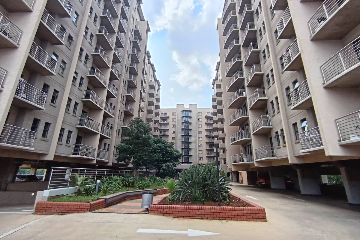 A view of the apartment complex courtyard featuring multi-story residential blocks with private balconies, paved walkways, and established garden beds.
