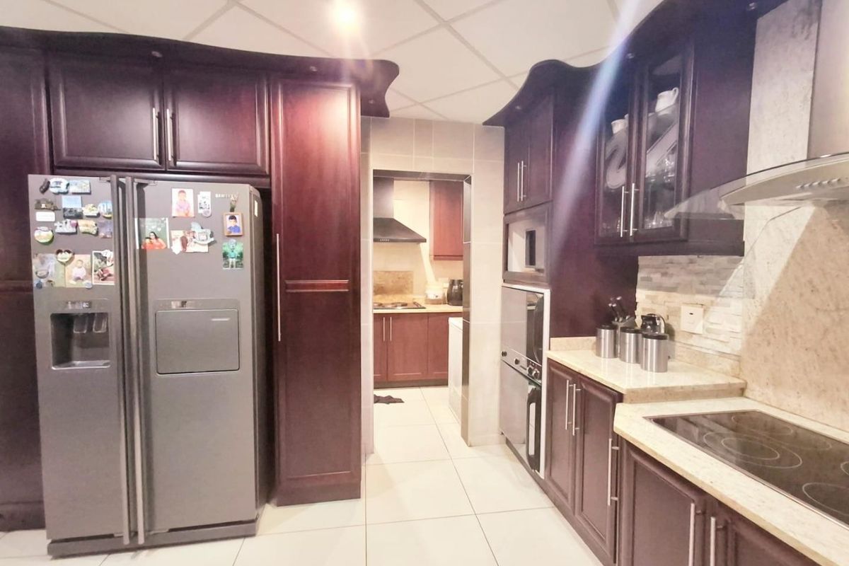 A well-appointed kitchen featuring dark wood cabinetry, stone countertops, integrated appliances, and a tiled backsplash, with an adjacent scullery area visible.