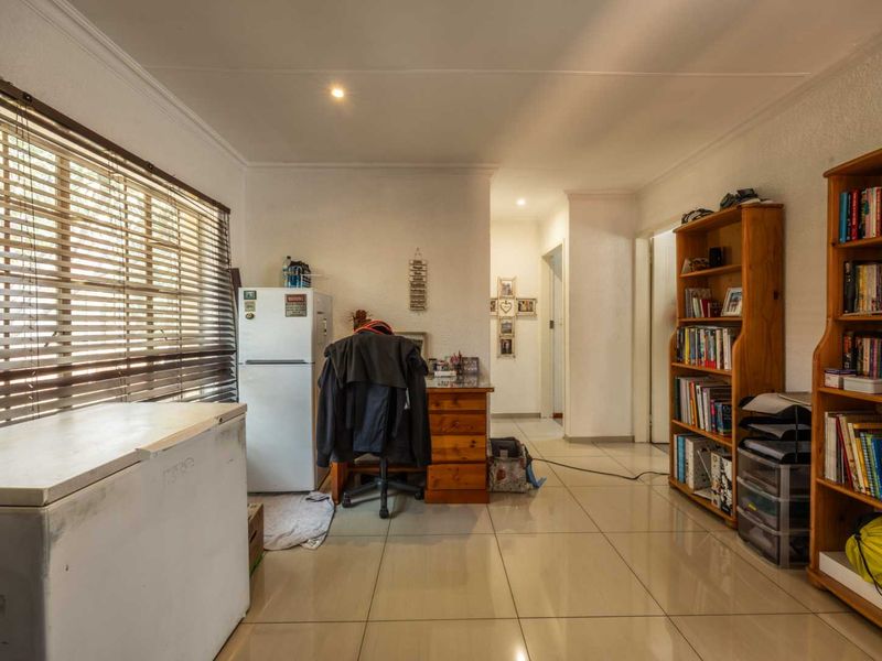 A functional living area featuring neutral tiled flooring, recessed downlighting, and large windows fitted with venetian blinds, offering a versatile space for various uses.