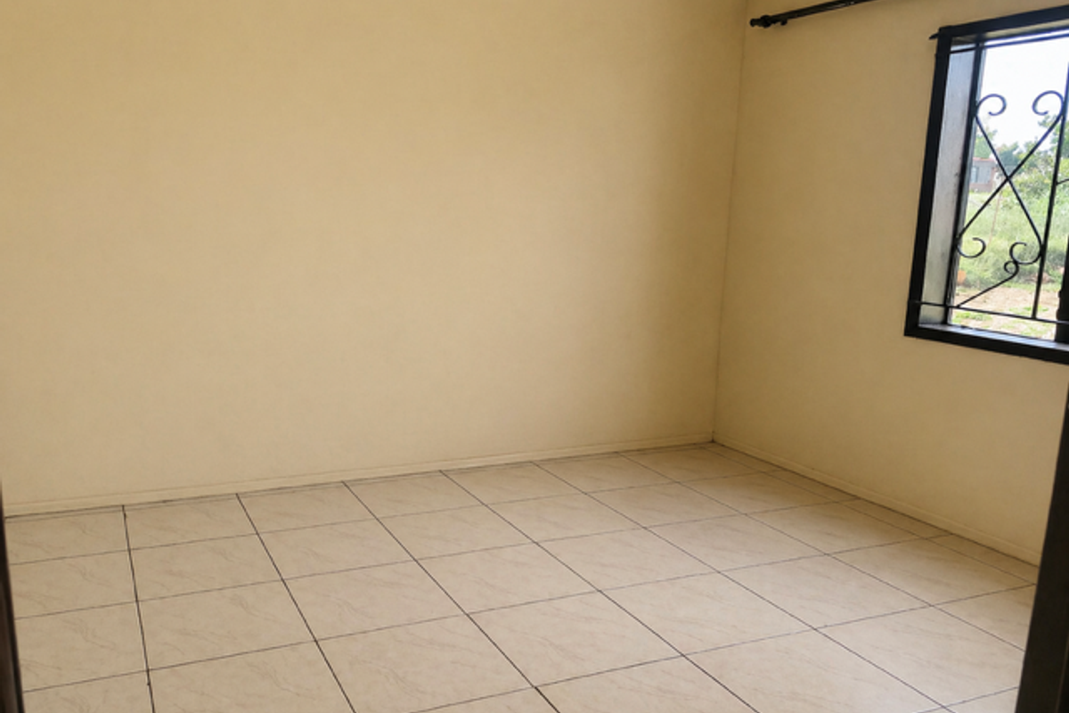 A vacant bedroom featuring neutral tiled flooring and a window fitted with security bars.