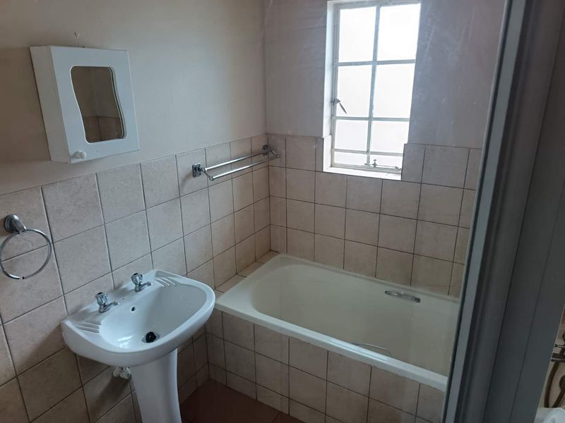 A functional bathroom featuring a pedestal basin, bathtub, and tiled splashback, requiring cosmetic updates to modernize the space.