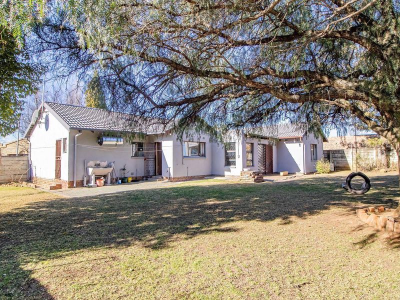 Rear view of the house featuring a spacious garden, concrete patio area, and established trees.