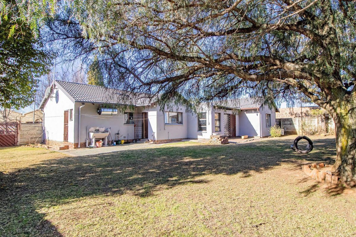 Rear view of the house featuring a spacious garden, concrete patio area, and established trees.