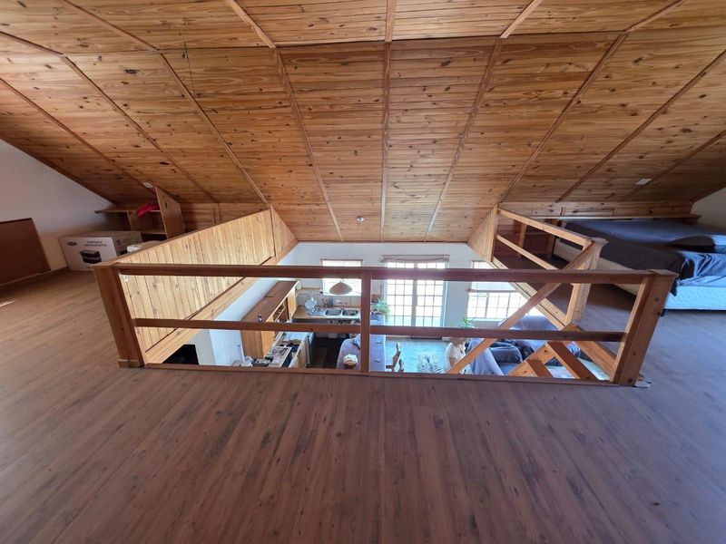 A spacious open-plan mezzanine level featuring timber-clad vaulted ceilings and laminate flooring, overlooking the main living and kitchen area below.