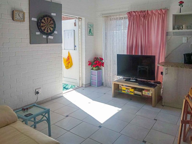 Open plan living area featuring painted brick walls and ceramic tiled flooring, with an integrated kitchen space and direct access to the exterior.