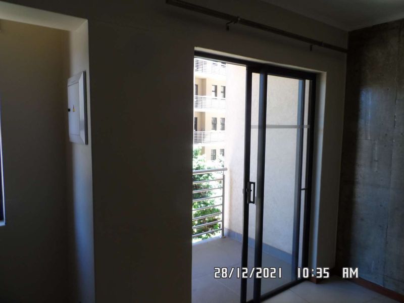 An empty living area featuring a sliding glass door leading to a balcony, with an exposed concrete feature wall and neutral finishes.