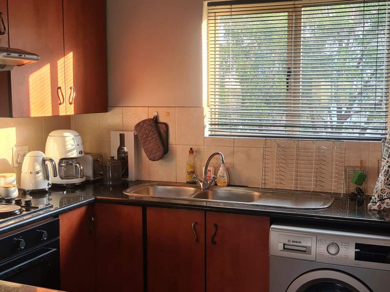 A functional kitchen featuring wood-finish cabinetry, dark laminate countertops, a built-in electric oven and hob, and a stainless steel sink with a window view.