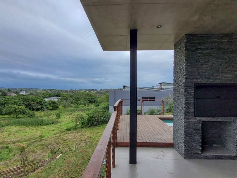 Covered balcony featuring a built-in stone-clad braai, timber decking, and a timber balustrade, offering expansive views over the surrounding landscape.