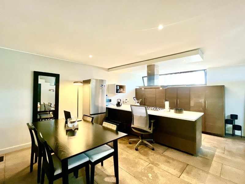 Modern open-plan kitchen and dining area featuring a central island with gas cooktop, sleek cabinetry, and stone countertops, finished with neutral floor tiles.