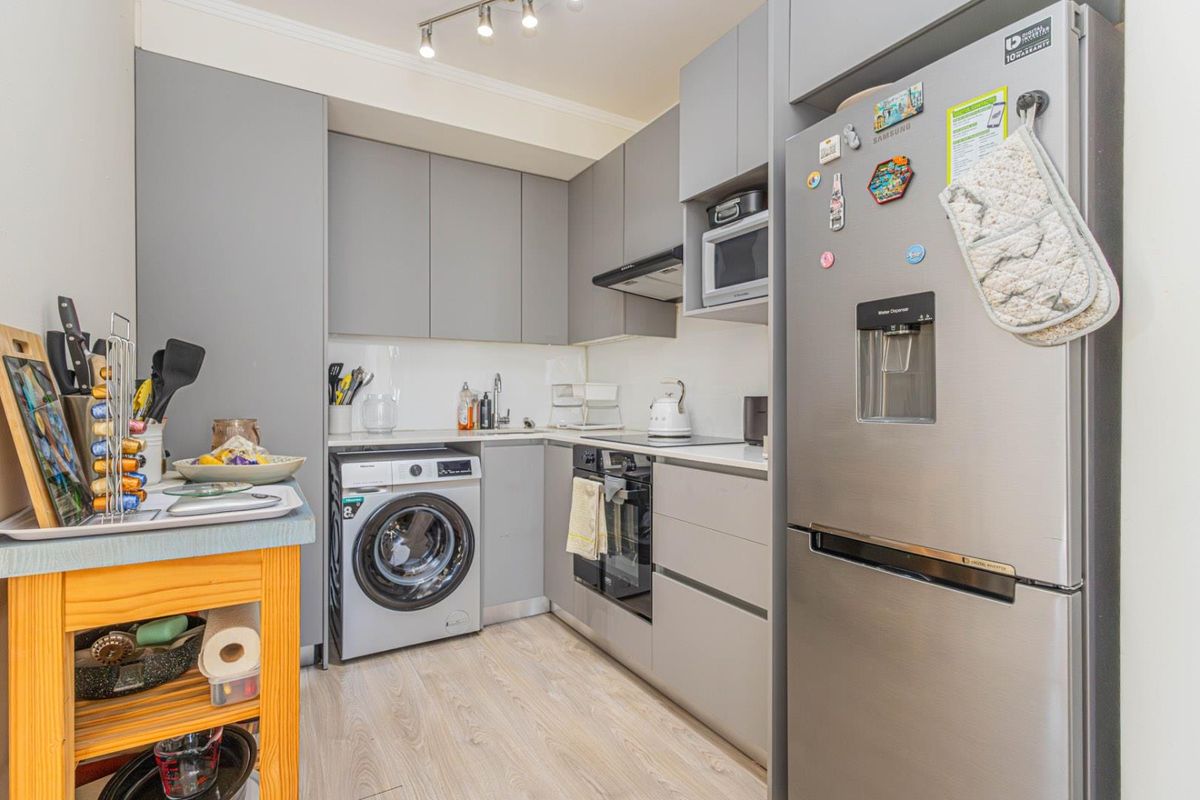 Compact modern kitchen featuring grey cabinetry, integrated oven, hob, extractor fan, built-in microwave, and a dedicated space for a washing machine.