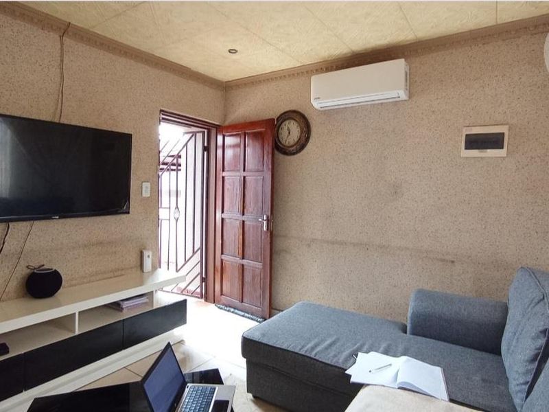 A living room featuring tiled floors, an air conditioning unit, and direct access to an exterior area through a timber door with a security gate.
