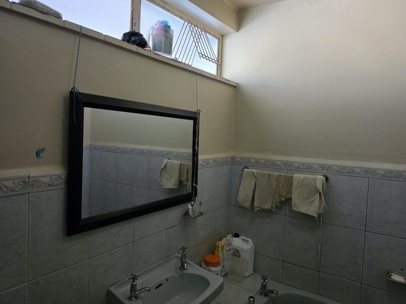 A dated bathroom featuring a pedestal basin, tiled walls, and a high-level window, requiring cosmetic updates to improve its overall condition and appeal.
