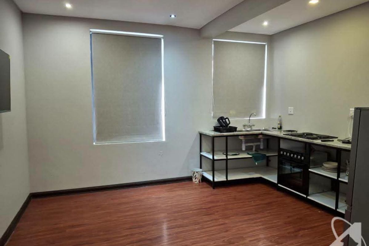 A clean, modern kitchen area featuring laminate flooring, recessed lighting, and an open-concept shelving unit with a built-in oven and hob.