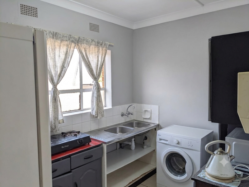 Compact kitchen area featuring a double stainless steel sink, tiled splashback, and built-in cabinetry with space for laundry appliances.